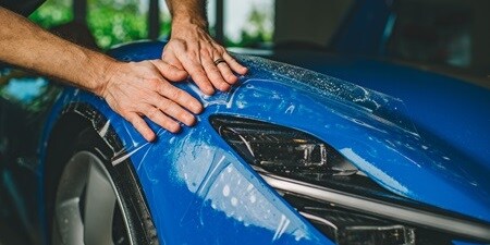 Personne appliquant un film de protection de peinture sur une voiture
