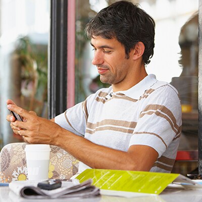 Image montrant un homme assis à une table regardant son appareil mobile
