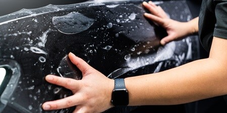 Personne appliquant un film de protection de peinture sur une voiture
